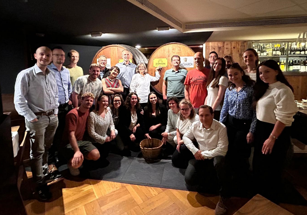 A mixed group of people posing in front of two large cider barrels.