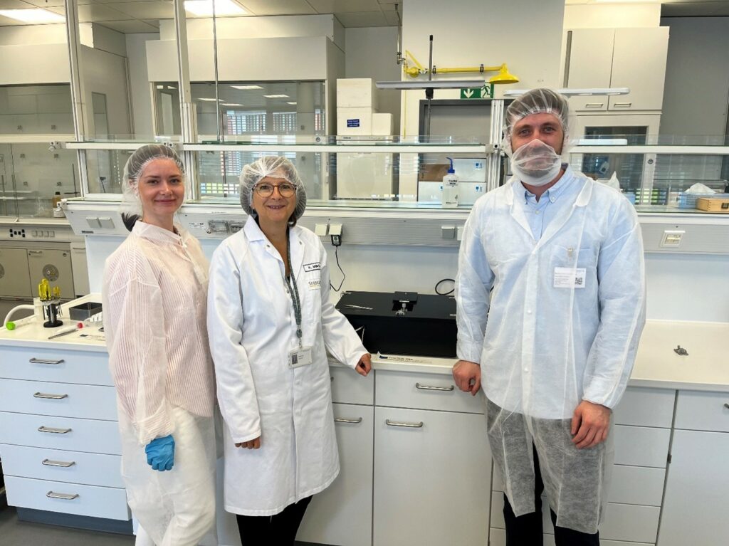 Two young researchers from university Ulm together with a representative from Seeberger pose in the lab in front of the photonics prototypes.