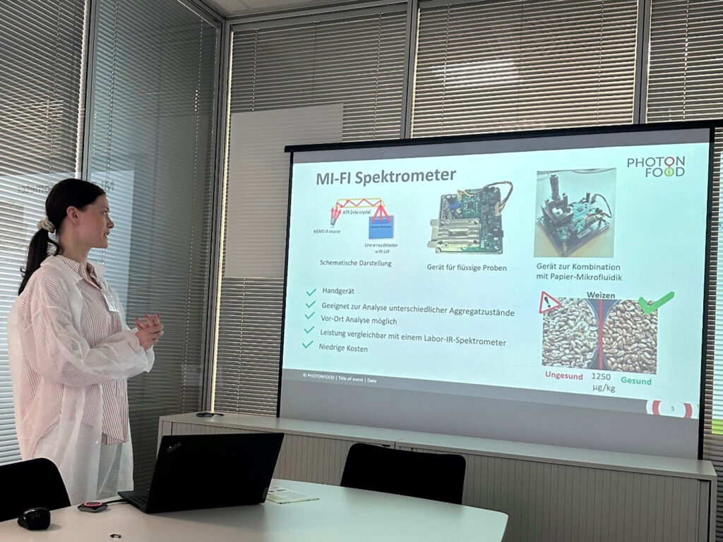 A young lady in protective gear presents in front of a large screen.